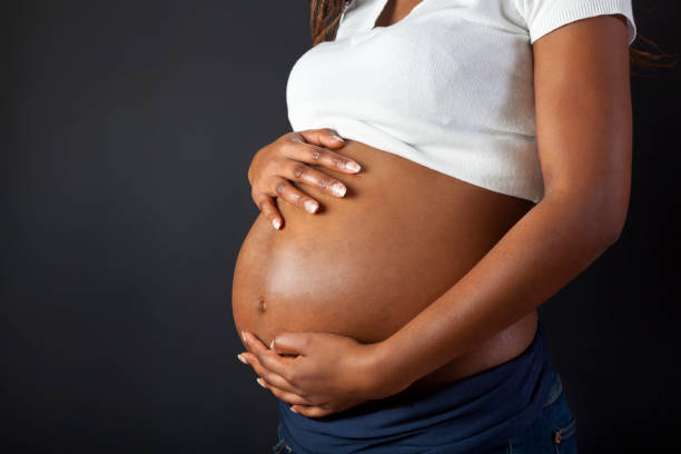 A pregnant African woman holding her belly on dark background.